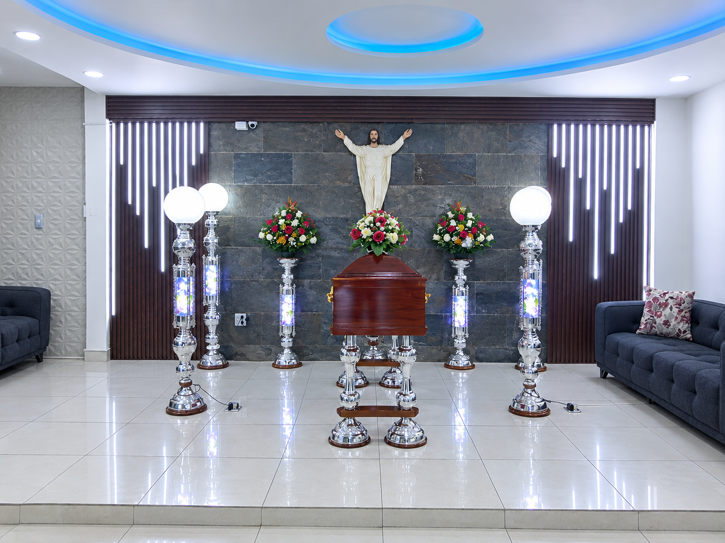 Sala de velación principal de Funeraria La América con iluminación cálida tenue, sillas tapizadas y decoración floral, ambiente solemne y recogido, tonos oscuros